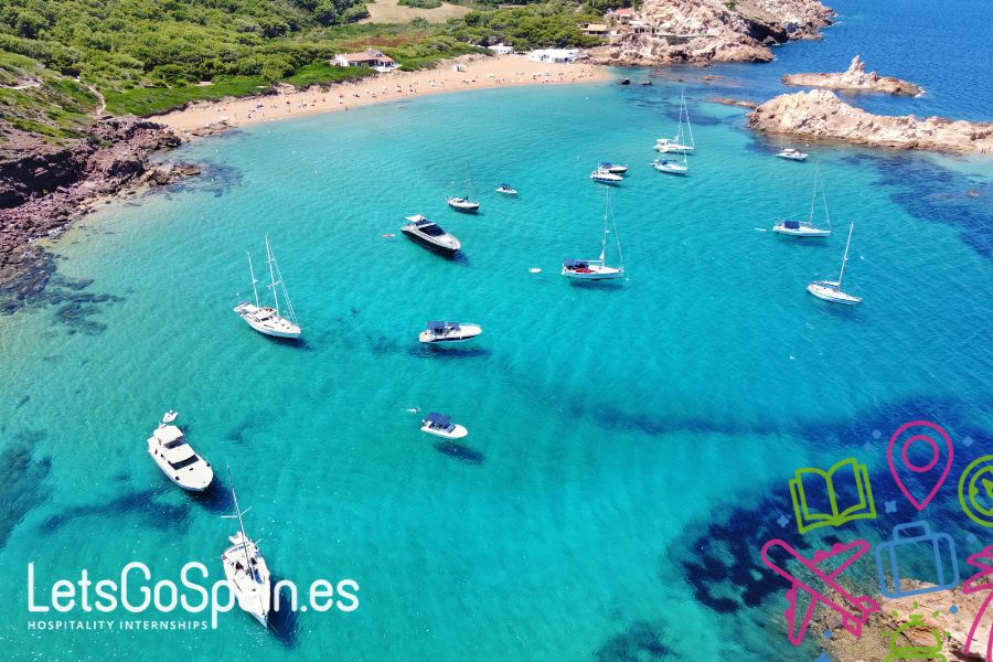 Boats in a clear blue bay near a sandy beach in Menorca, Spain